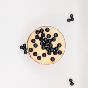 K&ouml;nnte beinhalten: Eine durchsichtige Glassch&uuml;ssel gef&uuml;llt mit einem hellorangen Dessert, das mit schwarzen Tapiokaperlen belegt ist.