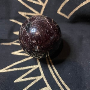 May include: A dark red and black sphere made of polished gemstone. The sphere is smooth and has a reflective surface.