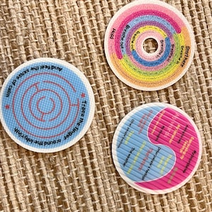May include: Three circular textured discs with instructional text. One features a rainbow spiral with breathing prompts. Another is a blue labyrinth with the text Trace the finger around the labyrinth and feel the sense of calm. The third is a pink and blue chart.