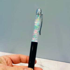 Op de afbeelding: Een zwarte en transparante pen met een zilveren dop. Het transparante deel van de pen is gevuld met kleurrijk glitter.
