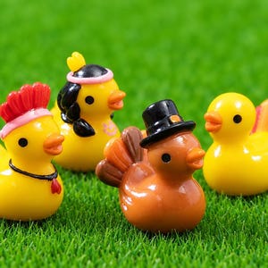 May include: Four miniature duck figurines. One yellow duck wears a red mohawk, one yellow duck has black hair with a pink headband, one brown duck wears a black top hat with a tail, and one yellow duck has a multi-colored tail.