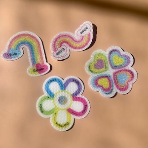 May include: Four glittery stickers with breathing exercise prompts. One is a rainbow with "Inhale" and "Exhale" text. Another is a wavy line with "Inhale" and "Exhale". A flower shape has "Start here", "Inhale", and "Exhale". A heart cluster has "Breathe".