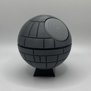 May include: A gray, spherical speaker shaped like the Death Star from Star Wars. The speaker has a round, black speaker grille on the side.
