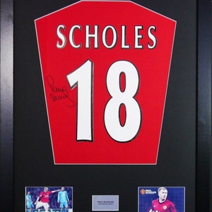 Könnte beinhalten: Ein gerahmtes rot-weißes Fußballtrikot mit dem Namen "SCHOLES" und der Nummer "18" auf der Vorderseite. Das Trikot ist von Paul Scholes signiert. Der Rahmen enthält zwei kleinere Fotos von Scholes beim Fußballspielen.
