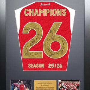 May include: Framed Arsenal Premier League Champions jersey with the number 26 and signatures. The jersey is red with white accents and the word "CHAMPIONS" in gold. Includes photos of the team and a plaque.