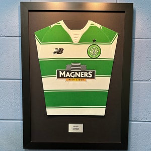May include: A framed green and white football shirt with the Celtic Football Club logo and the Magners Irish Cider logo. The shirt is signed by Henrik Larsson.