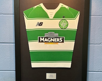 May include: A framed green and white football shirt with the Celtic Football Club logo and the Magners Irish Cider logo. The shirt is signed by Henrik Larsson.