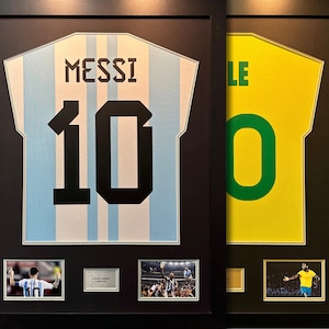 May include: Two framed soccer jerseys, one light blue with white stripes and the number 10 with the name "MESSI" above it, and the other yellow with a green number 10. Both jerseys are framed with black frames and include smaller photos of the players.
