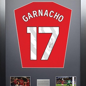 Könnte beinhalten: Ein gerahmtes rotes Fußballtrikot mit dem Namen "GARNACHO" und der Nummer "17" in Weiß. Das Trikot ist mit schwarzer Tinte signiert. Der Rahmen enthält zwei kleinere Fotos des Spielers in Aktion.
