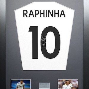 May include: A framed white soccer jersey with the name "RAPHINHA" and the number "10" in black. The jersey is signed by the player. There are two smaller photos of the player in action on either side of the jersey.