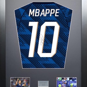 Può includere: Un'esposizione incorniciata con una maglia da calcio blu con il nome MBAPPE e il numero 10 stampati in bianco. La maglia include una firma, due fotografie d'azione di un calciatore e una piccola targa con testo all'interno di una cornice nera.
