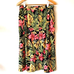 May include: A vintage skirt with a vibrant tropical floral print. The skirt features a black background with pink flowers, yellow and green leaves. The skirt is hanging on a wooden hanger.