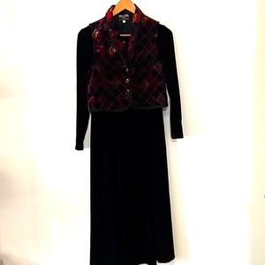 May include: A black velvet dress with long sleeves, paired with a quilted vest featuring a burgundy and gold floral pattern. The vest has a button-up front and is hanging on a wooden hanger.