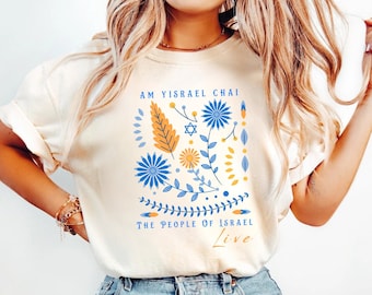 Puede incluir: Una camiseta blanca con un diseño floral y el texto "Am Yisrael Chai The People of Israel Live".