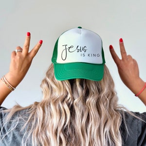 K&ouml;nnte beinhalten: Eine wei&szlig;e und gr&uuml;ne Trucker-Kappe mit dem Text "Jesus is King" in schwarzer Schrift.