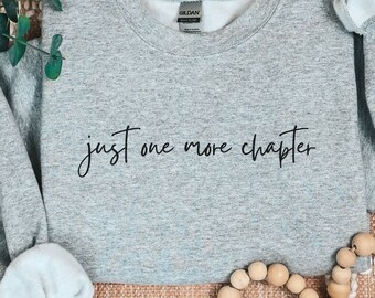 May include: Gray sweatshirt with the text "just one more chapter" in black script font.