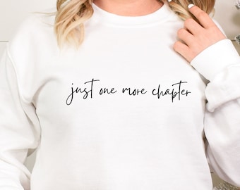 May include: White sweatshirt with the text "just one more chapter" in black script.