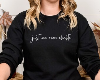 May include: A black sweatshirt with the text "just one more chapter" in white lettering.