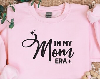May include: Pink sweatshirt with black text that reads "In My Mom Era" with stars on either side of the text.