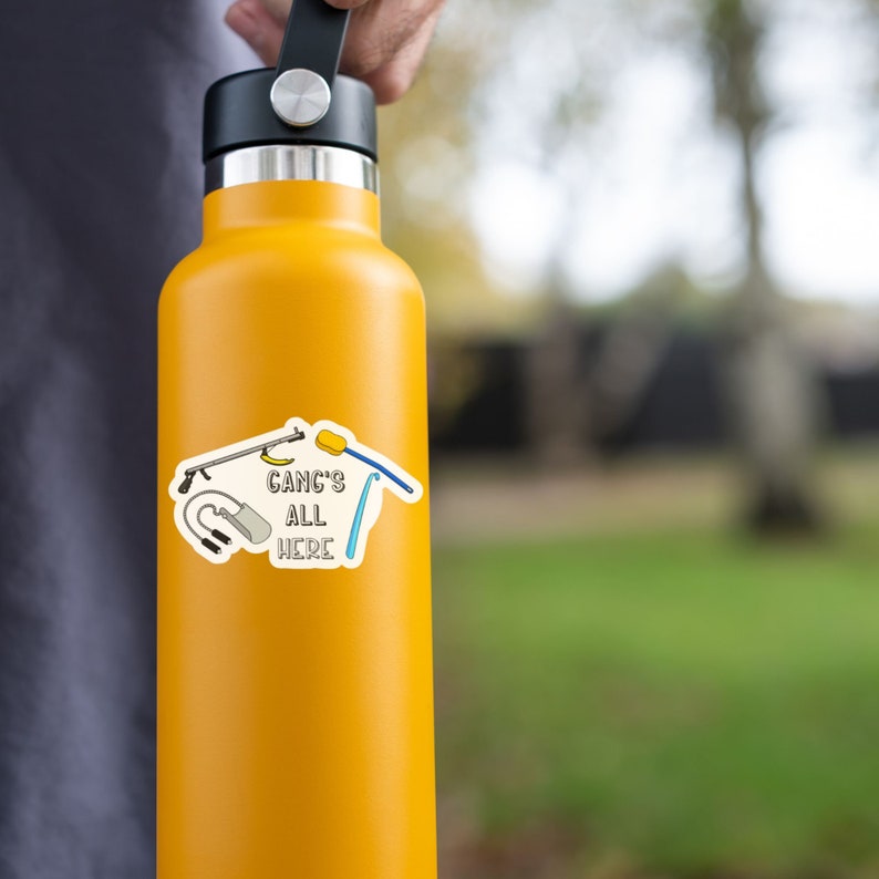May include: A yellow water bottle with a sticker that says "Gang's All Here" and features a cartoon illustration of a sponge, a razor, a shower head, and a squeegee.