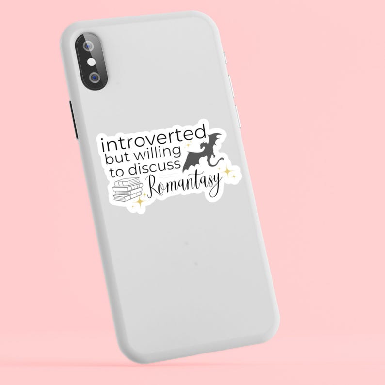 May include: White iPhone case with a black and white sticker that says "introverted but willing to discuss romantasy" with a silhouette of a dragon and a stack of books.
