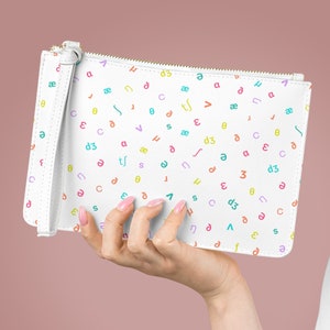 May include: White clutch purse with a zipper closure and a wrist strap. The purse is covered in a pattern of colorful letters and symbols.