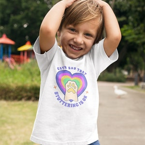 May include: A white t-shirt with a rainbow heart and a paw print in the center. The text "Cats Say That Stuttering Is Ok" is written around the heart.