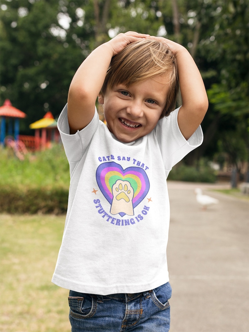 May include: A white t-shirt with a rainbow heart and a paw print in the center. The text "Cats Say That Stuttering Is Ok" is written around the heart.