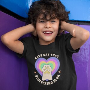 May include: A black t-shirt with a rainbow heart and paw print graphic. The text on the shirt reads "Cats Say That Stuttering Is Ok."