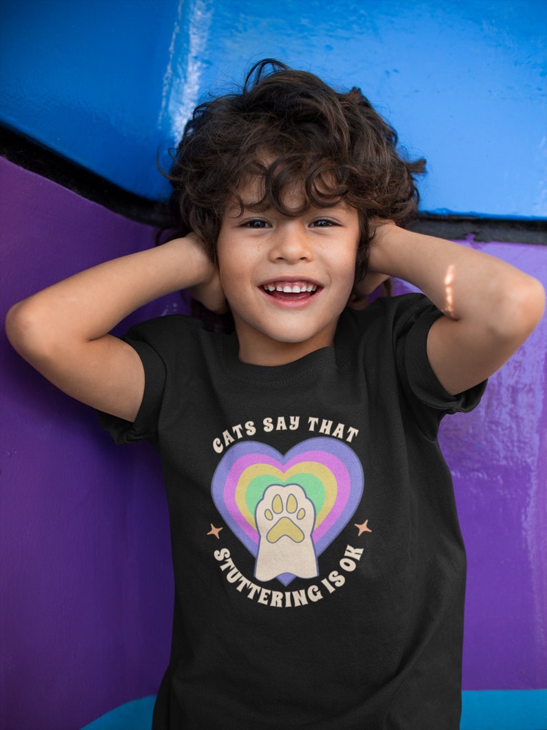 May include: A black t-shirt with a rainbow heart and paw print graphic. The text on the shirt reads "Cats Say That Stuttering Is Ok."