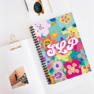 May include: A spiral bound notebook with a colorful floral pattern and the word "SLP" in white, bubble letters. The flowers are in shades of pink, yellow, orange, blue, and green.