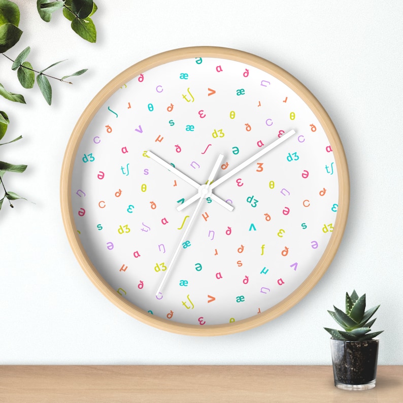 May include: A white clock with a wooden frame and white hands. The clock face is covered in a random pattern of colorful letters and symbols.
