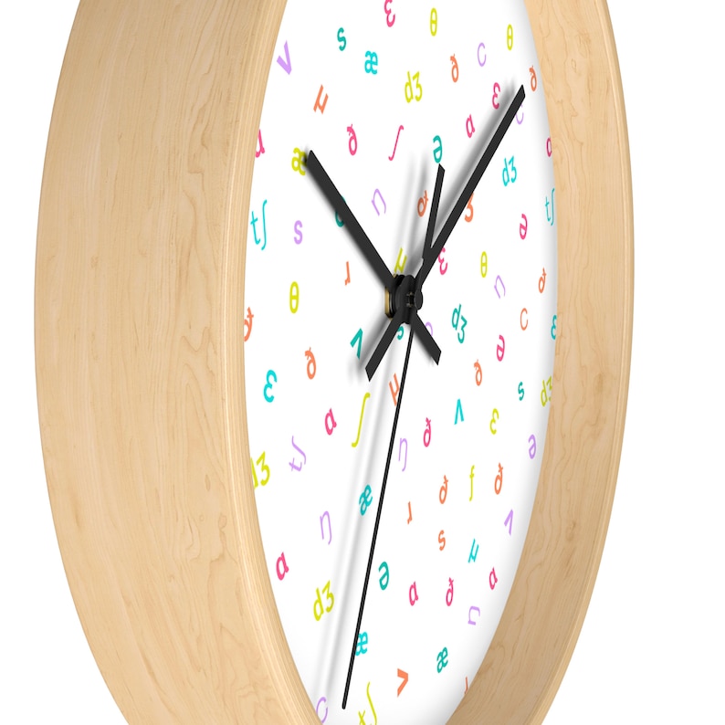 May include: A white clock face with black hands and a wooden frame. The clock face is covered in a random pattern of colorful letters and symbols.