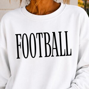 May include: A white crewneck sweatshirt featuring the word FOOTBALL printed in large, bold, black capital letters across the chest. The garment has long sleeves with ribbed cuffs and a ribbed neckline, constructed from a solid white fabric.