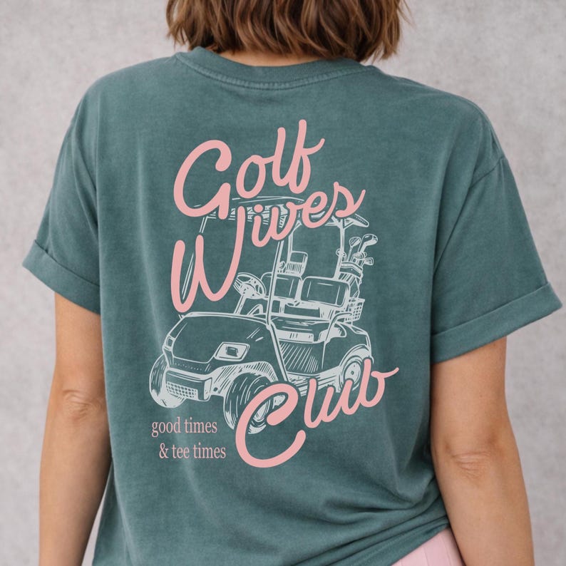 May include: Teal-colored t-shirt with a graphic of a golf cart and the words "Golf Wives Club" in pink script. The phrase "good times & tee times" is printed below the cart.