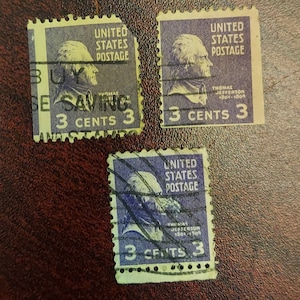 May include: Three vintage United States postage stamps featuring a portrait of Thomas Jefferson. Each stamp is purple and yellow and reads "United States Postage" and "3 Cents 3".