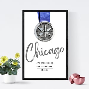 Pode incluir: Impressão emoldurada com uma medalha da Maratona de Chicago suspensa por uma fita azul. A medalha prateada exibe "Chicago Marathon" e os anos "1977" e "2023". Abaixo, a palavra "Chicago" está escrita em itálico, com a data, o nome e a hora.