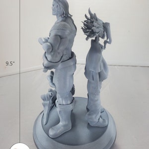 K&ouml;nnte beinhalten: Eine 3D-gedruckte graue Figur von zwei Charakteren, die auf einem runden Sockel stehen. Der Charakter links ist eine muskul&ouml;se Figur mit H&ouml;rnern und einem Umhang. Der Charakter rechts ist eine kleinere Figur mit stacheligem Haar. Der Sockel hat einen Durchmesser von 15,2 cm und die Figur ist 24,1 cm hoch.