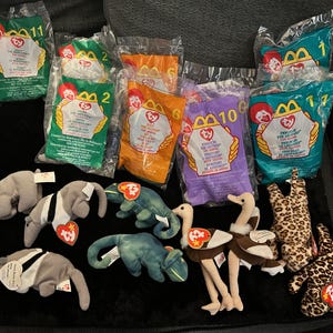 May include: A collection of Ty Beanie Baby plush toys, including various animals like anteaters, lizards, and ostriches, alongside sealed McDonald's Happy Meal bags. The bags are in various colors and feature the McDonald's logo and numbers.