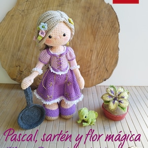 Puede incluir: Pascal el camaleón de crochet, una sartén y una flor mágica. La flor está en una maceta. El conjunto es morado, verde y marrón.  Pascal, sartén y flor mágica (Muñeca Rapunzel no incluida)