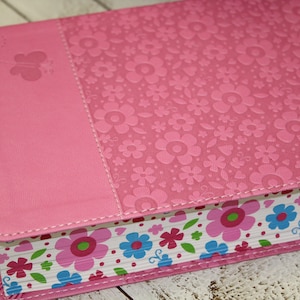 May include: A pink hardcover journal with a floral pattern and a butterfly design. The journal has a white and pink floral pattern on the edges.