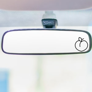 Puede incluir: Un espejo retrovisor con un contorno negro de un melocotón con una hoja en la parte superior.