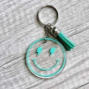 May include: A turquoise blue smiley face keychain with lightning bolt eyes and a silver key ring with a turquoise tassel.