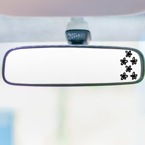 May include: A black rearview mirror with a cluster of small black flower decals on the right side of the mirror.