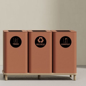 May include: Three brown metal bins with labels for trash, recycle, and compost. Each bin has a black circle with a symbol and text.