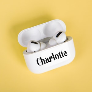 Può includere: Auricolari wireless bianchi in una custodia bianca con il nome "Charlotte" scritto sul davanti.