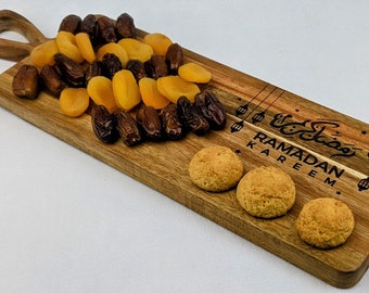 May include: A wooden serving board with a Ramadan Kareem inscription, decorated with dates, dried apricots, and cookies.