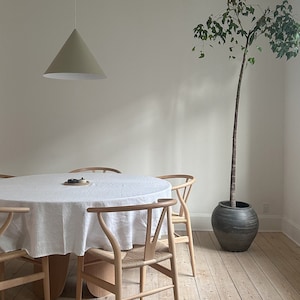 May include: A white tablecloth covers a round wooden dining table with four wooden chairs. A green potted plant stands in the corner of the room.