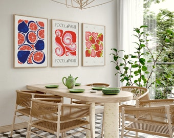 May include: Three framed prints with colorful illustrations of fruit. The prints are hung on a white wall above a dining table with four chairs. The prints feature a red and blue grapefruit, a red and pink octopus, and a red and green strawberry.