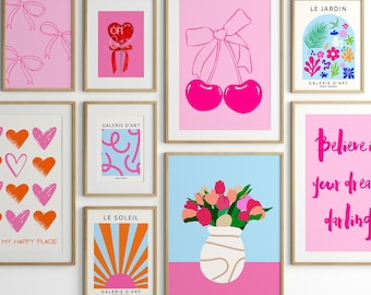 May include: A collection of nine framed prints featuring various designs, including hearts, bows, cherries, flowers, and a sunrise. The prints are all in pink, orange, and blue colours and have the text "GALERIE D'ART" and "LE JARDIN" on them.